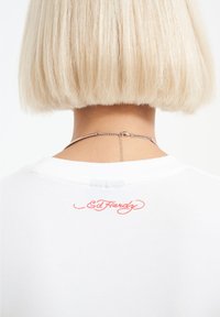 Bílý tričko s výšivkou červeného loga "Ed Hardy" na zadním výstřihu; hladký bavlněný materiál; kulatý límec; krátké rukávy.