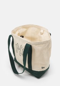 Sac fourre-tout en toile avec des sangles vertes, corps crème et initiales brodées bien visibles. Comprend une bague intérieure et des coutures durables.