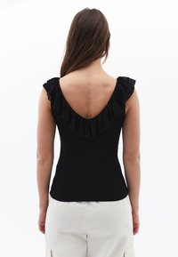Mustapaitainen ilmanhihaisen toppi, jossa on pitsireunainen kaula-aukko ja syvä V-mallinen selkäosa, muotoilu on lähellä vartaloa ja siinä on pehmeä tekstuuri.