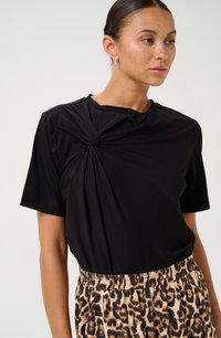 Haut noir à manches courtes avec un design tordu à l'avant, associé à un short à taille élastique imprimé animal. Texture lisse sur l'ensemble.