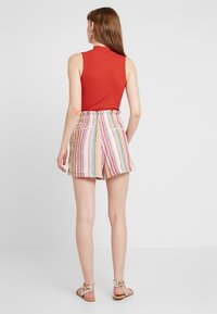 Top senza maniche rosso abbinato a pantaloni corti a righe multicolori con vita elastica e due tasche laterali. Sandali piatti con cinturini.