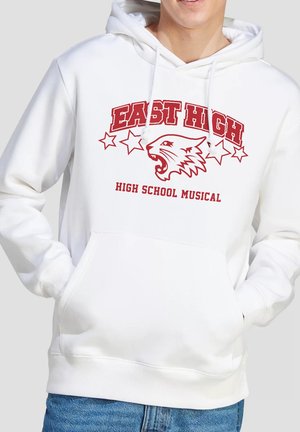 Person wearing white hoodie with red "East High High School Musical" text, stars, and a roaring wildcat logo on the front. Hands in pockets.