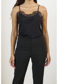 Camisola nera con pizzo lungo il collo, caratterizzata da sottili spalline. Abbinata a pantaloni neri a vita alta. Texture liscia.