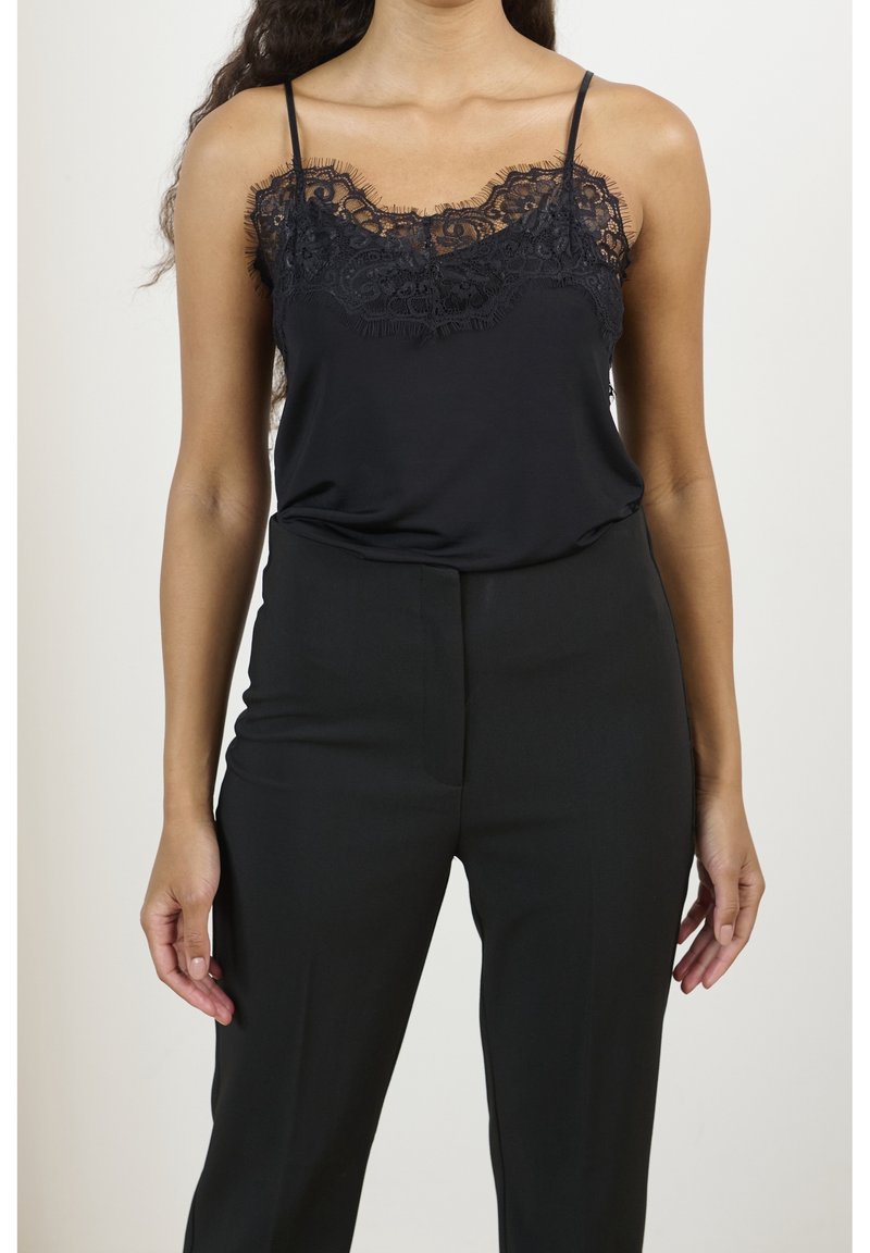 Camisola nera con pizzo lungo il collo, caratterizzata da sottili spalline. Abbinata a pantaloni neri a vita alta. Texture liscia.