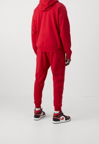 Sweat-shirt rouge à capuche et pantalon de jogging rouge assorti. La tenue présente une coupe décontractée avec des poignets côtelés, accompagnée de baskets noires et rouges.