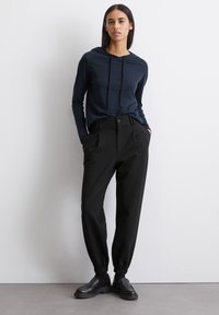 Marineblauwe hoodie met lange mouwen, gecombineerd met zwarte elastische taillebroek, met een relaxte pasvorm en minimalistisch ontwerp, aangevuld met zwarte schoenen.