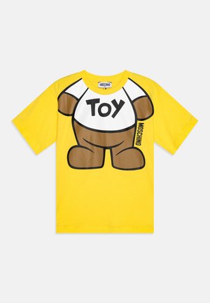 Gelbes Baumwoll-T-Shirt mit einem Cartoon-Teddybär-Graphic, auf einem weißen Bereich mit dem Wort "Spielzeug" in fetten schwarzen Buchstaben.