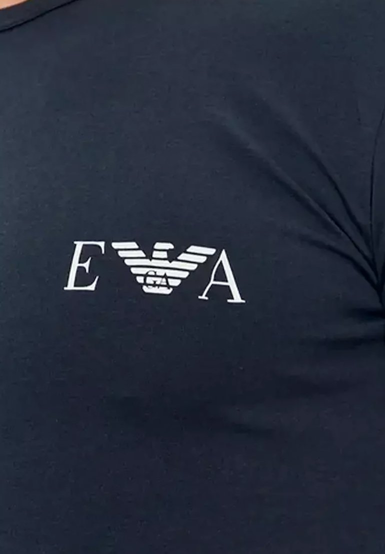 Tummansininen puuvillapaita, jossa on valkoinen logo tyyliteltyine siipineen ja rinnassa painettuna kirjaimet "EVA". Klassinen malli, lyhyet hihat.