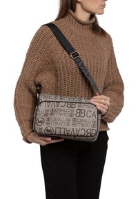 Borsa a tracolla beige con stampa nera del logo, forma rettangolare, chiusura con zip e tracolla regolabile. Tessuto testurizzato con dettagli del brand.