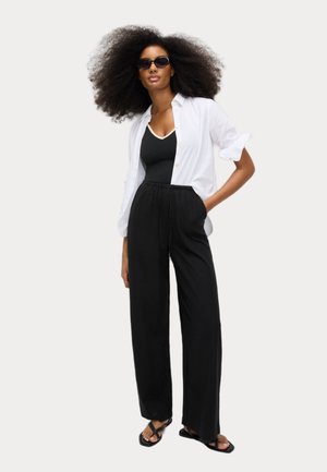 Black wide-leg pants with an elastic waist, paired with a white button-up shirt and a black tank top. Accessories include dark sunglasses.