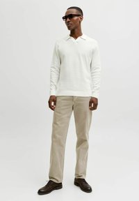 Chemise blanche à manches longues texturée avec col ; pantalon en velours côtelé beige clair ; chaussures marron foncé ; lunettes de soleil rectangulaires noires.