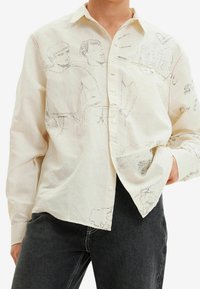 Camicia bianca in cotone con illustrazioni a contorno in filo nero, dettagli in cucitura rossa e una vestibilità ampia e rilassata.