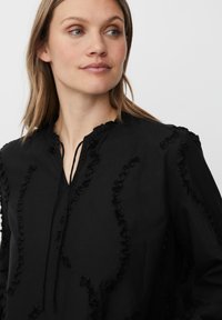 Blusa nera con morbidi dettagli a volant lungo le cuciture, scollatura a v e vestibilità rilassata. Realizzata in tessuto leggero.