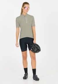 Maillot de cyclisme à manches courtes, gris clair, avec des rayures verticales et une fermeture éclair à l'avant, assorti à un short noir et un casque noir dans les mains.