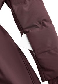 Mouw van een bordeauxrode donzen jas met een gladde textuur, voorzien van een met rits afsluitbaar zakje waarin een wit kaartje zichtbaar is. De buitenkant is van waterafstotende stof.