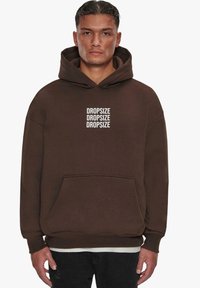 Brauner Kapuzenpullover aus weichem Stoff mit einer vorderen Tasche und Bündchenärmeln. "DROPSIZE" mehrfach in Weiß auf der Vorderseite aufgedruckt.