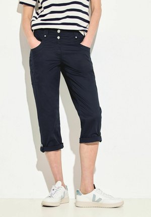 Pantalons cropped navy avec ourlets retournés, dotés de poches et d'une fermeture à bouton sur le devant. Portés avec des sneakers blanches et un haut rayé. Texture lisse.