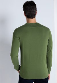 Long-sleeve green shirt in soft fabric, featuring a round neck, fitted design, and smooth texture. No visible patterns or embellishments.