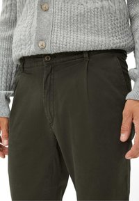 Grijze gebreide trui met structuurpatroon en beige knopen, gecombineerd met donkergroene chino's met een rechte voorkant en zijzakken.
