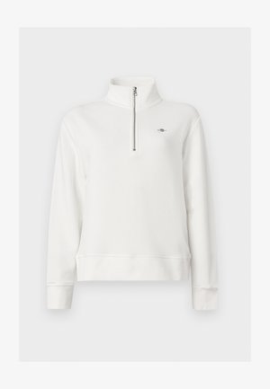 Jersey blanco de manga larga con cremallera de un cuarto en la parte delantera y cuello alto, con un pequeño logo bordado en el pecho izquierdo.