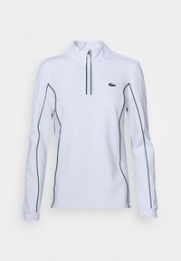 Suéter blanco de manga larga con cuello de cremallera, que presenta un ribete en contraste verde a lo largo de las mangas y el cuerpo, y un pequeño logo en el pecho.