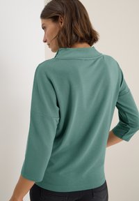 Suéter de manga larga, color verde claro, con cuello y mangas tres cuartos; textura suave y diseño sencillo.