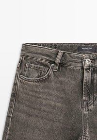Black denim jeans with a faded texture, featuring a five-pocket design, metal button closure, and a label from Massimo Dutti.