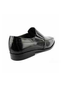 Zapato negro de piel tipo slip-on con un acabado suave, punta redondeada y un tacón bajo. Presenta costuras mínimas y un diseño simple y elegante.