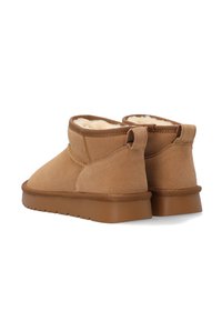 Pair of tan suede ankle boots with shearling lining and flat brown rubber soles, viewed from the back on a white background.
