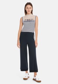 Gestreiftes ärmelloses Oberteil in Weiß und Marineblau mit hohem Kragen, kombiniert mit Marineblau weiten Hosen und weißen Sneakers mit braunen Sohlen.