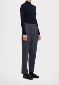 Maglione a collo alto a costine blu navy, pantaloni a gamba larga grigi con texture e vita elasticizzata, mocassini neri con dettagli in metallo dorato.