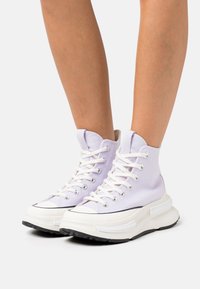 Sneakers alte in tela lavanda chiara con lacci bianchi, suola nera a contrasto e dettagli testurizzati sulla suola e sulla linguetta.