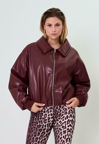 Giacca bomber in ecopelle bordeaux con grande colletto, zip frontale e polsini a coste, abbinata a leggings con stampa animale. 