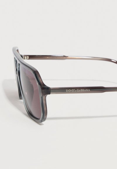 Μαύρα διαφανή τετράγωνα γυαλιά ηλίου με σκουρόχρωμους φακούς και λογότυπο "Dolce & Gabbana" στο πλευρικό μπράτσο.