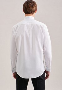 Camicia bianca a maniche lunghe con orlo arrotondato, polsini con bottone e colletto classico. Tessuto liscio con una leggera lucentezza.