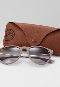 Ochelari de soare Ray-Ban cu un cadru mat de culoare roz deschis și lentile gri cu gradient, însoțiți de un etui din piele texturată de culoare maro.
