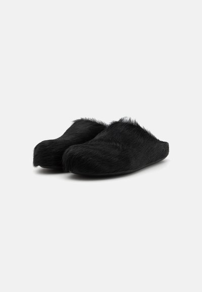 Papuci de casă slip-on căptușiți cu blană neagră, cu o formă rotundă și textură moale. Partea superioară are o finisare pufoasă pentru confort.