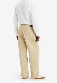 Pantalones cargo de algodón beige con un corte holgado, que cuentan con dos bolsillos traseros, una etiqueta de parche en la cintura y detalles de costura en contraste.