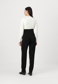 Pull blanc avec un tricot texturé, associé à un pantalon noir taille haute, avec une finition lisse et une coupe droite. Bottines noires.