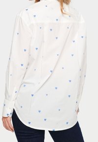Camicia bianca con bottoni, caratterizzata da motivi a cuori blu, maniche lunghe, orlo curvo e dettagli sui polsini. Tessuto morbido con un design classico.