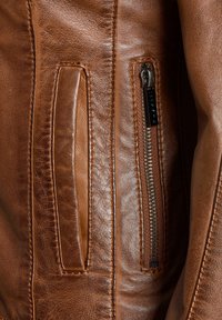 Bruine leren jack met een ritszak, een soepele textuur en gestikte accenten. De stof heeft een licht glanzende afwerking.