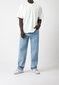Witte oversized t-shirt, lichtblauwe baggy jeans en grijze sneakers met witte accenten. Eenvoudig ontwerp met een relaxte pasvorm.