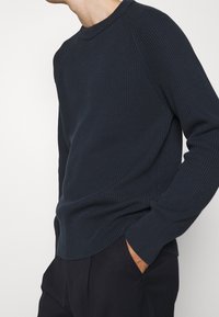 Mörkblå ribbad stickad tröja med rund halsringning, raglanärmar och en avslappnad passform, kompletterad med subtil textur.