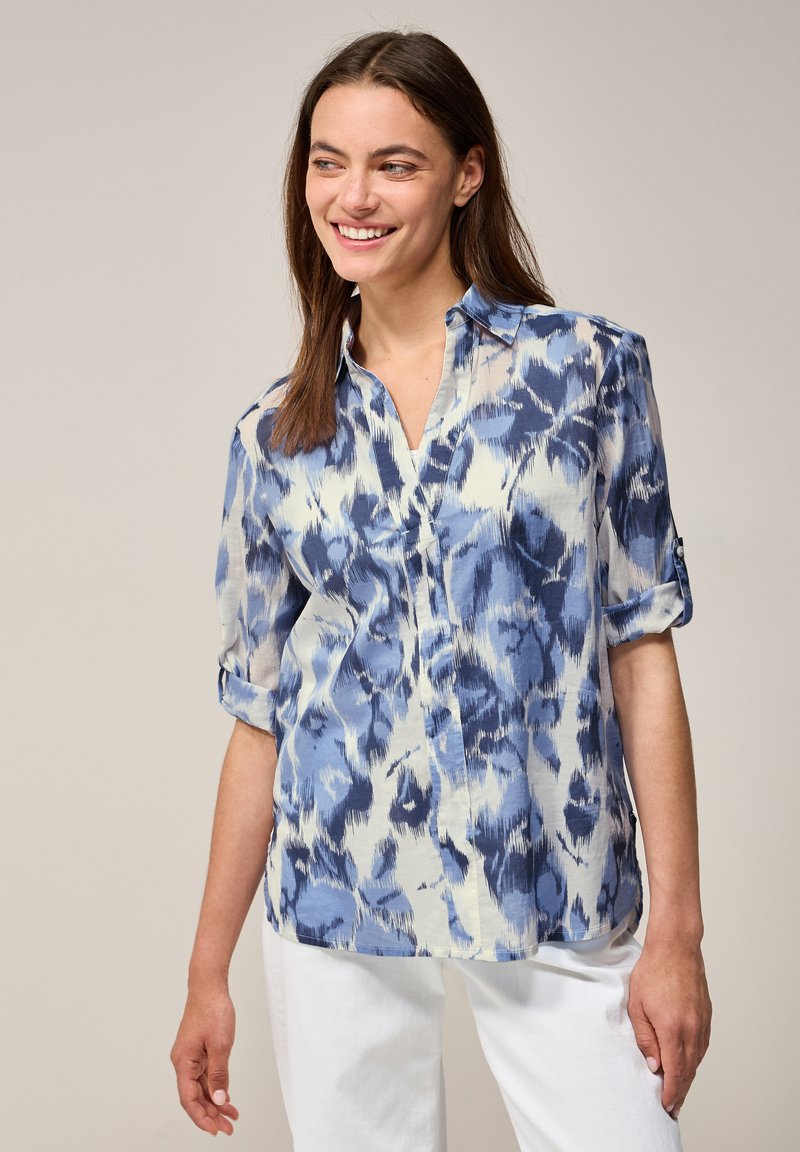Blusa de patrón azul y blanco con cuello y mangas enrolladas, hecha de una tela ligera con una textura suave.