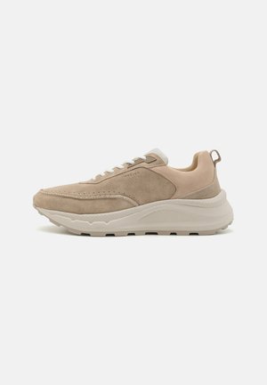 Beige sneakers with suede and smooth leather upper, textured details on the sole, and white laces. Pull tab at heel for easy wear.
