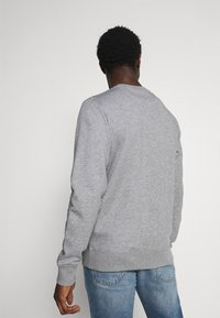 Sudadera gris de cuello redondo con puños y dobladillo acanalados, hecha de una tela suave. La vista trasera muestra un diseño simple sin logotipos ni patrones.