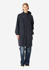 Granatowa wodoodporna parka z kapturem, dwiema przednimi kieszeniami, prostym krojem i regulowanymi sznurkami, w połączeniu z niebieskimi dżinsami i casualowym obuwiem.