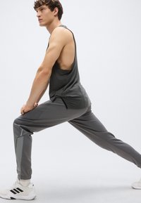 Pelēks sporta krekls bez piedurknēm ar atvērtu muguru, kopā ar pelēkām sporta biksēm ar gaiši pelēkām detaļām. Izskatu papildina balti sporta apavi.