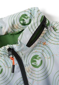 Giacca leggera con un design bianco e verde caratterizzato da motivi circolari e grafiche di dinosauri. Chiusura con zip con un accento arancione.