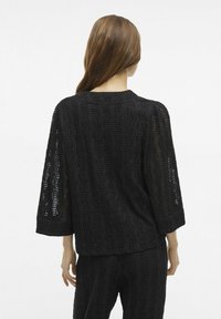 Maglia nera lavorata a maglia con un motivo a onda testurizzato, maniche a tre quarti e scollatura rotonda, abbinata a pantaloni testurizzati coordinati.